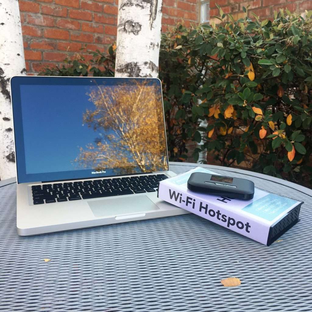 Wi-fi hotspot sitting on top of it's case next to a laptop.