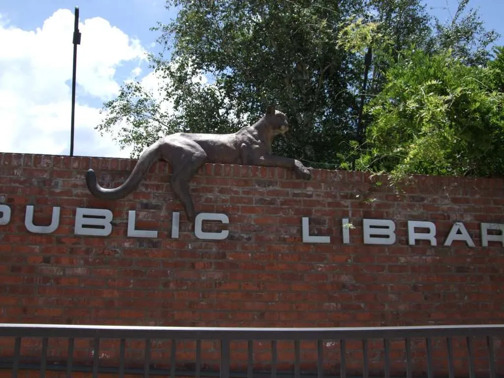 bronze mountain lion on top of wall  with "Prescott Public Library" metal letters underneath 