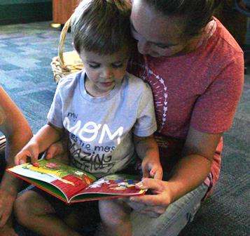 actively engaged mother sitting on floor reading picture book to preschool aged child who is on her lap